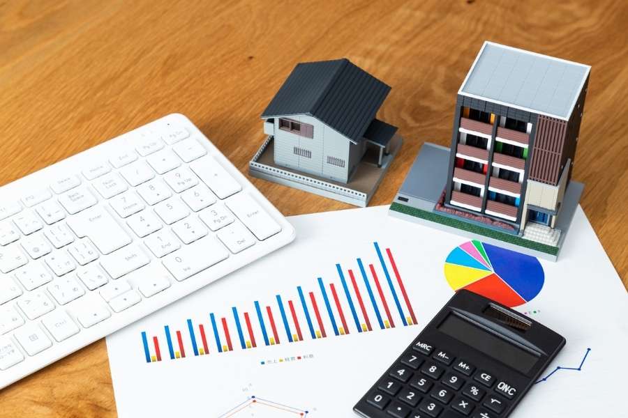 Un bureau avec un clavier, des graphiques financiers et des modèles de maisons pour bien préparer son état des lieux immobilier.