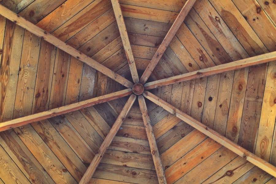 Une charpente en bois géométrique vue d'en bas avec des poutres rayonnantes formant des moulures de plafond en bois